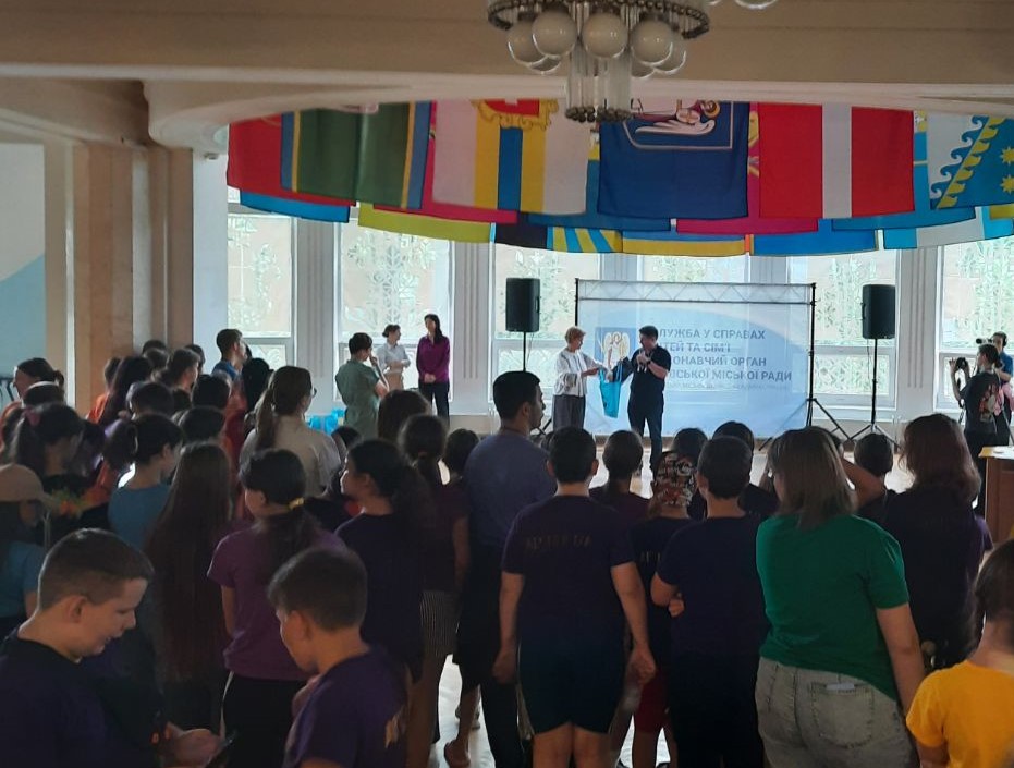 На фото організатори біля банера навпроти підлітків- учасників